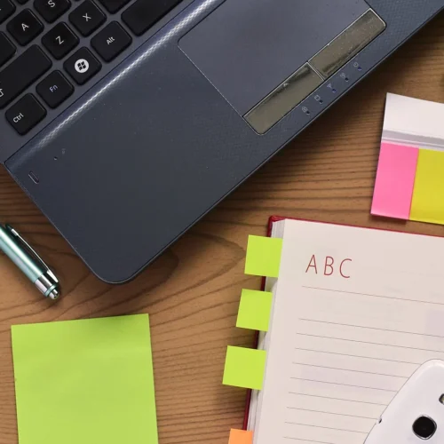 Notebook, pen and laptop arranged on a desk for writing and planning.