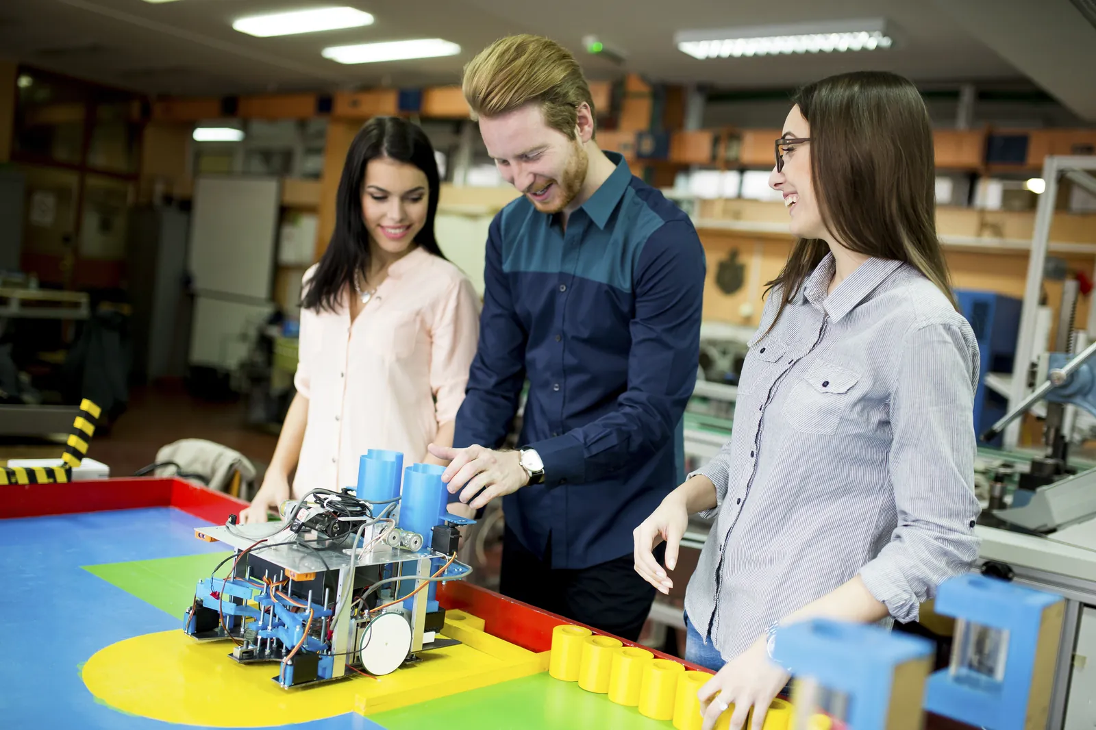 Three young adults examining a small robotics project at a workbench.