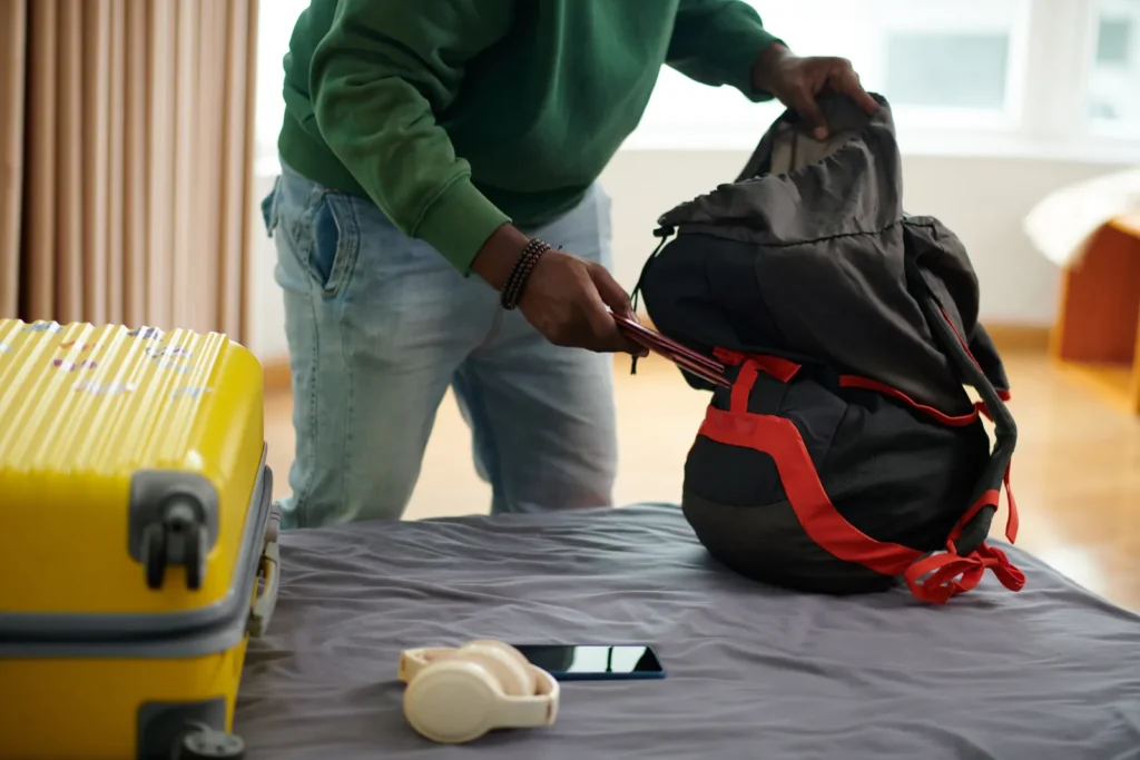 A traveller packing a backpack beside a suitcase at home.