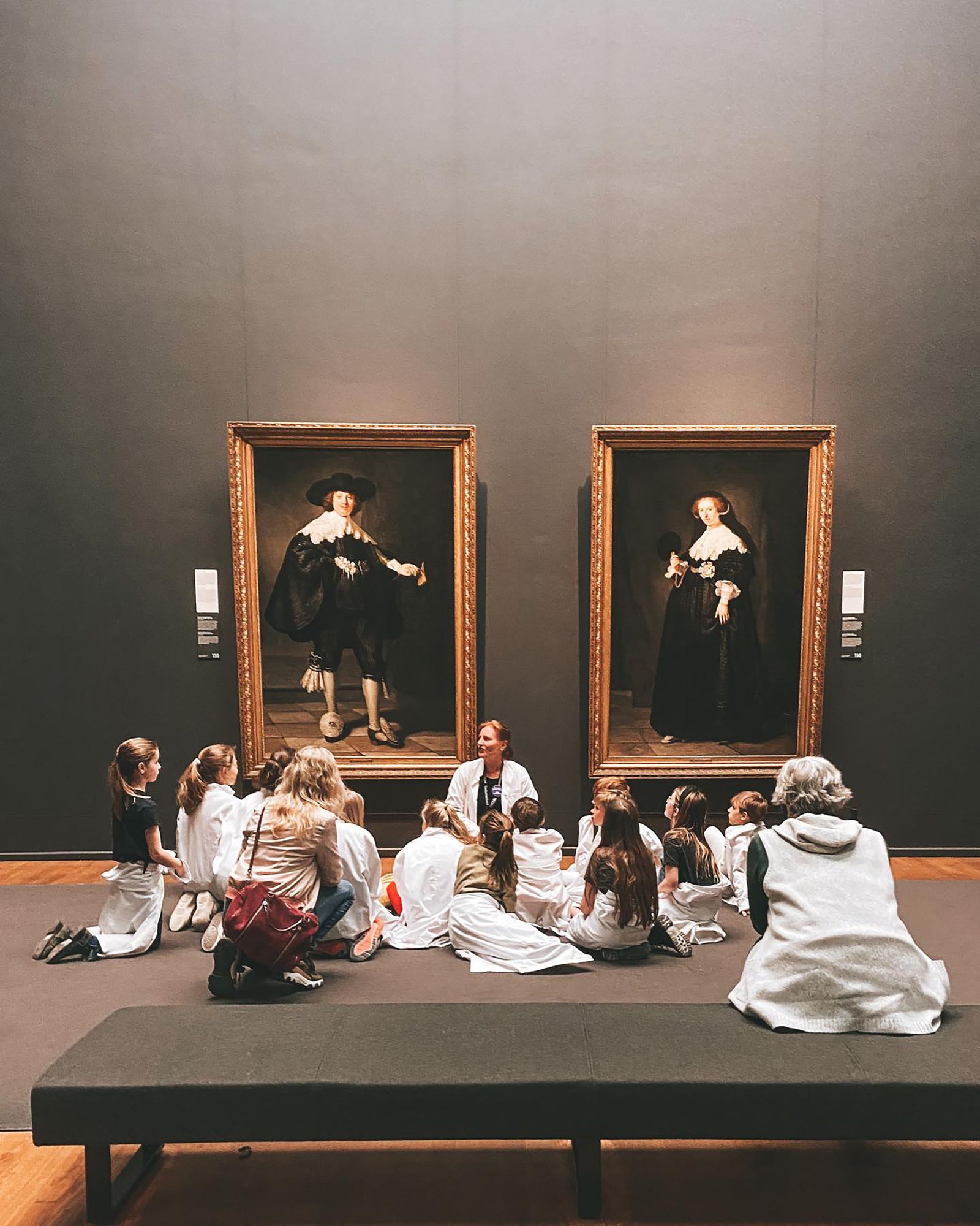 A teacher and children viewing paintings in a museum.