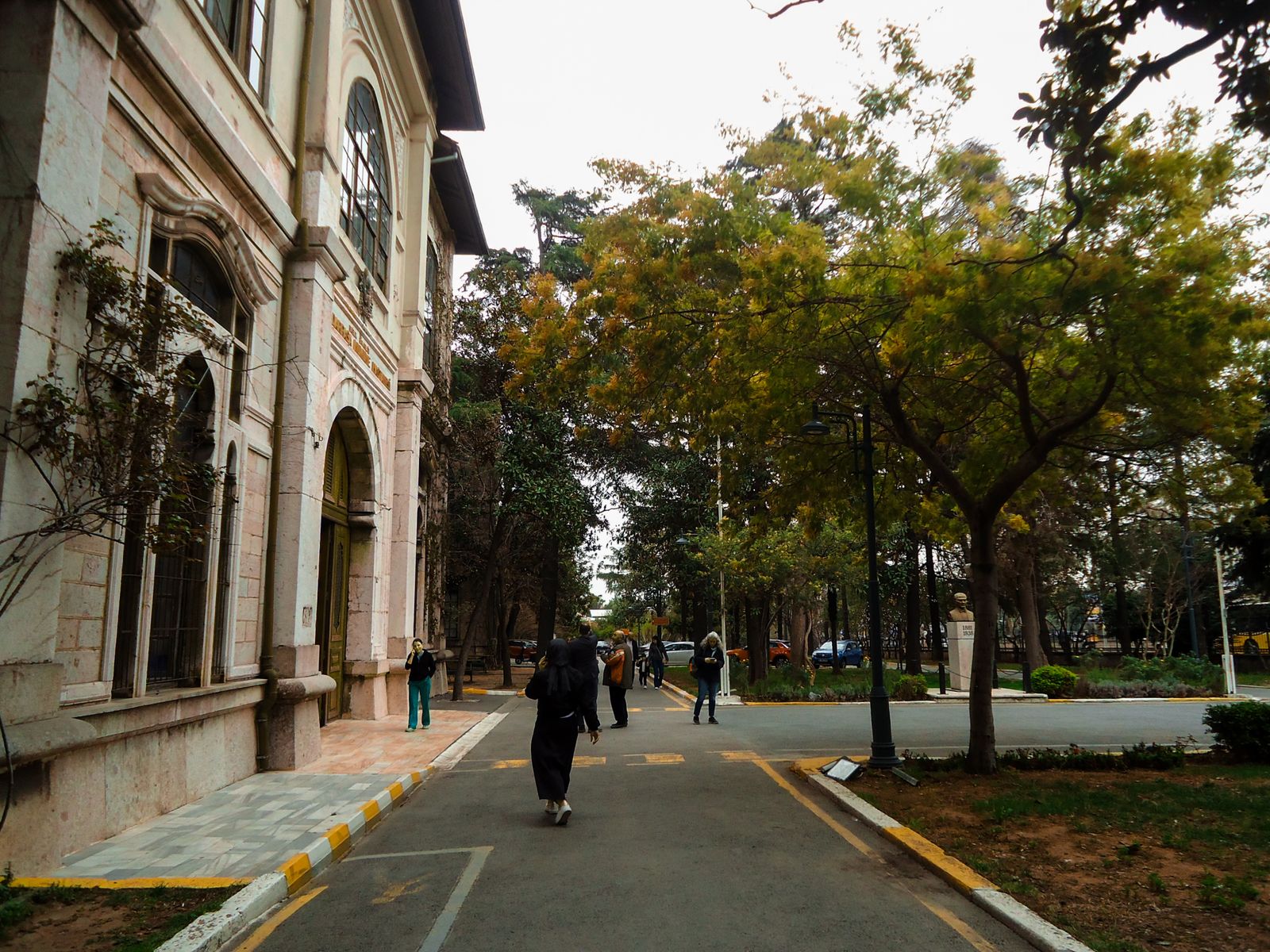 People walking between a historic university building and trees.