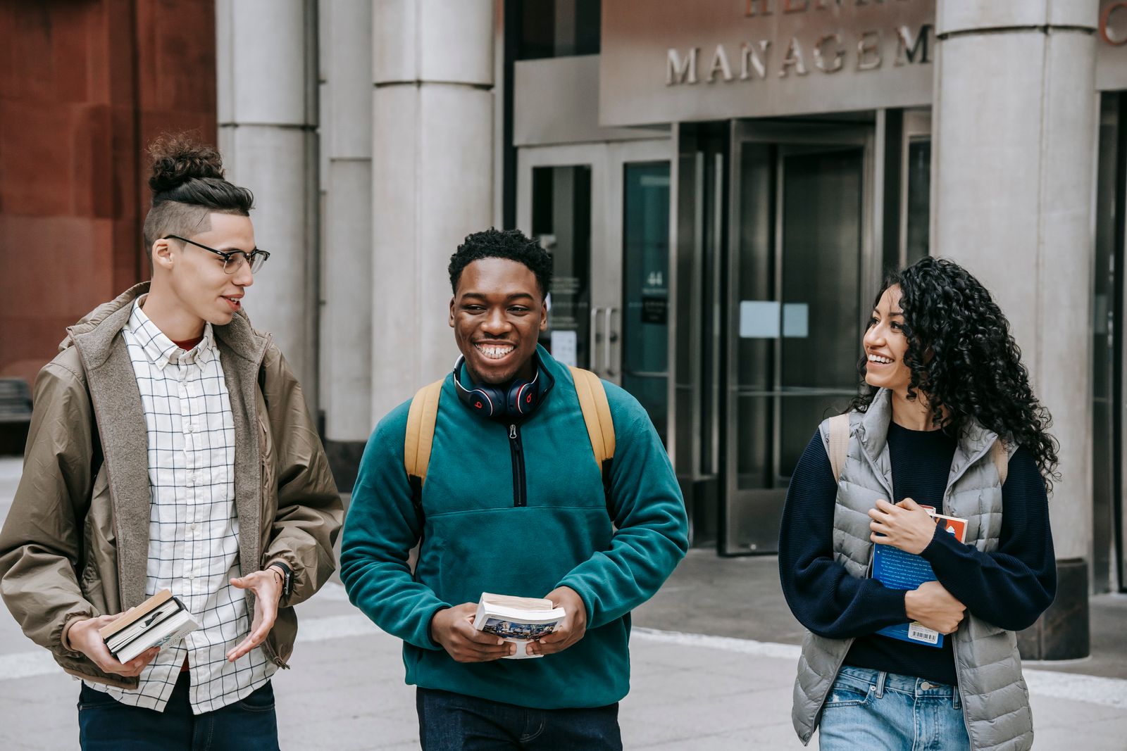 Students carrying books and talking outside an academic building.