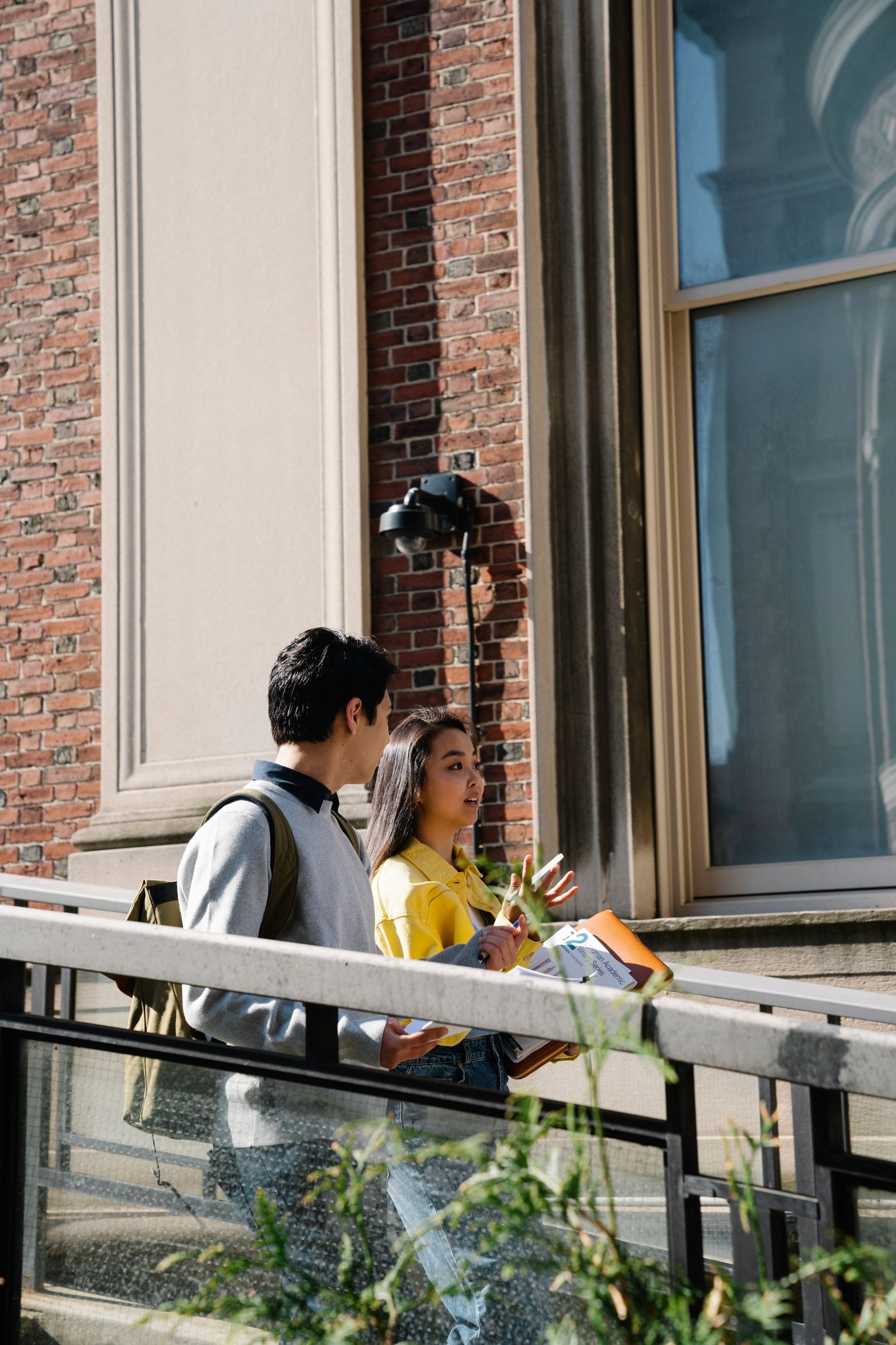 Two students walking beside a brick university building.