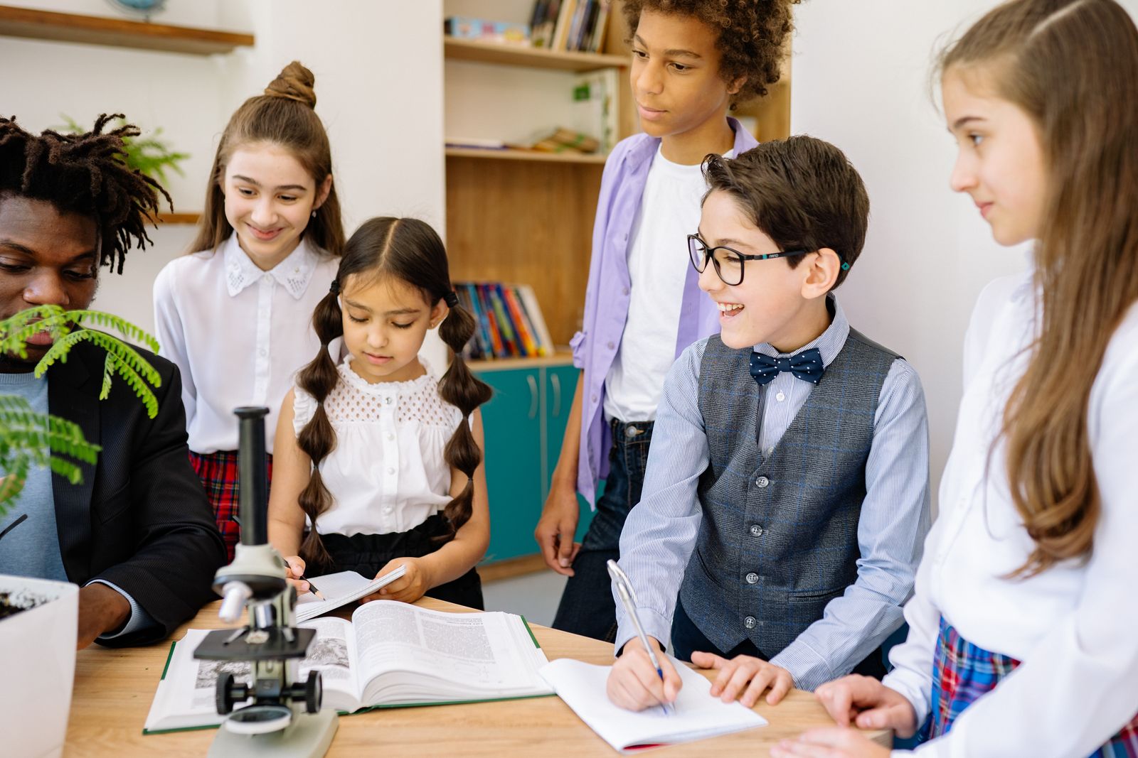 Children and a teacher examining a microscope together.